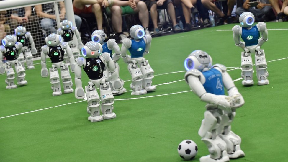 Robot memainkan pertandingan sepak bola.